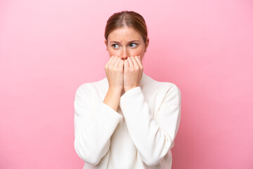 Young caucasian woman isolated on pink background nervous and scared putting hands to mouth
