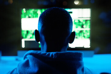 Soon all your information will be mine. Rearview shot of a male hacker cracking a computer code in the dark.