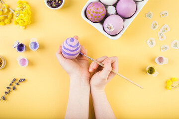 Child hands decorate Easter eggs on yellow background. Happy easter concept.