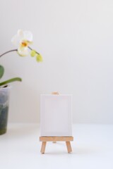 Minimalistic simple natural light mock up template. Empty space for text, logo, design. Stand for booklets, invitation, label with white paper, wooden tent card. Potted orchid on a table in a frame.