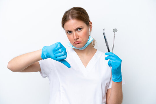 Dentist caucasian woman holding tools isolated on white background showing thumb down with negative expression