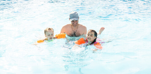 Happy family playing in blue water of swimming pool on a tropical resort at the sea. Summer vacations concept.