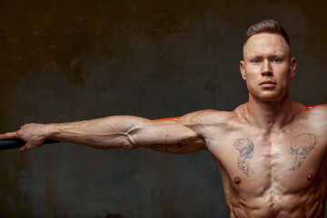 A fighter shirtless in black shorts, stands in a fighting artificially pose and holds a fight stick...