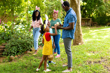 Naklejka premium Happy african american siblings wearing bunny ears with family in backyard on easter day