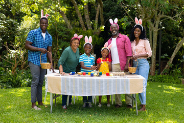 Fototapeta premium Happy african american multigenerational family in bunny ears with easter eggs in backyard