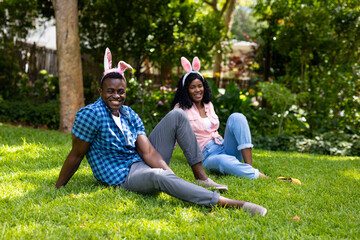 Naklejka premium Portrait of happy african american mid adult couple wearing bunny ears while sitting in backyard