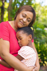 African american senior woman embracing granddaughter with eyes closed in backyard