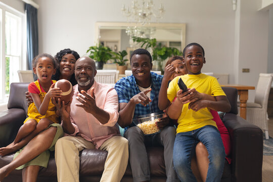 African american multi-generational family cheering while watching rugby match together on tv