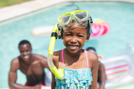 Portrait of smiling african american girl with snorkel while family in swimming pool on sunny day