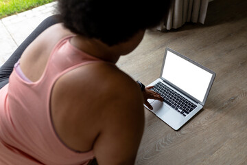 Rear view of african american mid adult woman using laptop while exercising at home - Powered by Adobe