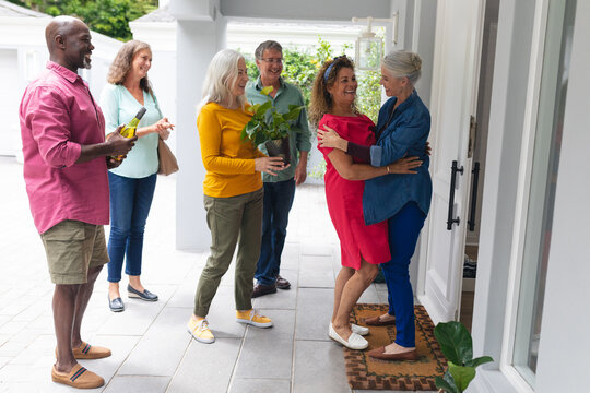 Happy Senior Woman Welcoming Multiracial Friends At Entrance During House Party