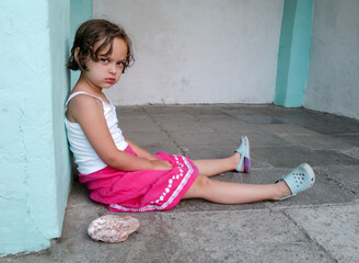 Cute angry girl is sitting on the floor, looking at the camera. Concept of children behavior problem