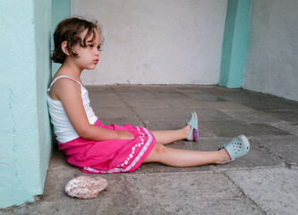 Cute angry girl is sitting on the floor near big stone. Concept of children behavior problem
