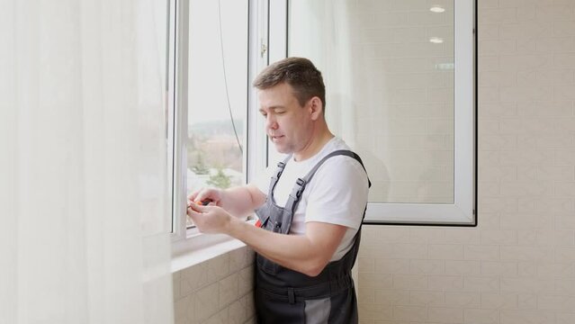 a repairman repairs, adjusts or installs metal-plastic windows in the apartment.