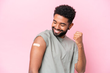 Young Brazilian man wearing a band aid isolated on pink background celebrating a victory