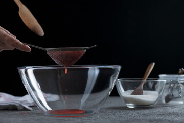 Woman straining strawberry jam through a sieve, home cooking and cooking concept