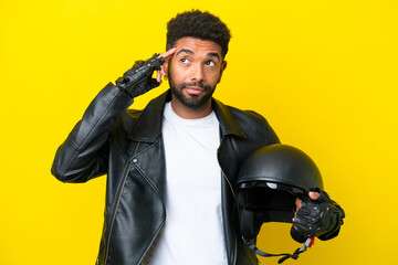 Young Brazilian man with a motorcycle helmet isolated on yellow background having doubts and...