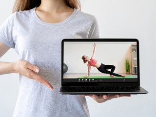 Virtual fitness class. Online training. Pilates tutorial. Woman hand recommending sport video program on laptop with athletic coach performing exercise on screen isolated on light.