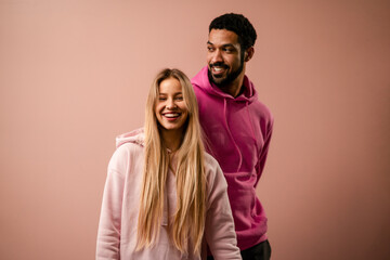 Fashion studio portrait of a happy young couple in hoodie posing over pink background. - Powered by Adobe