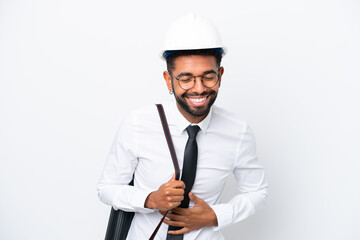 Young architect Brazilian man with helmet and holding blueprints isolated on white background smiling a lot