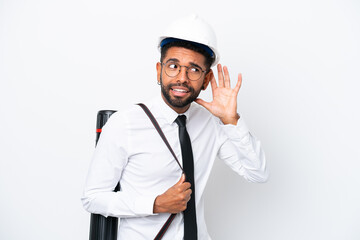 Young architect Brazilian man with helmet and holding blueprints isolated on white background listening to something by putting hand on the ear