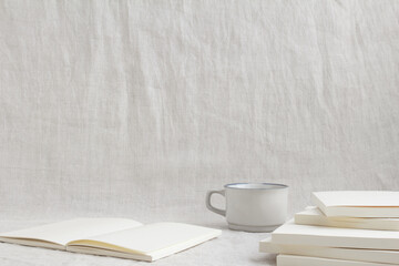 クリーム色のノートと白いマグカップが置かれたテクスチャのあるグレーの布の背景