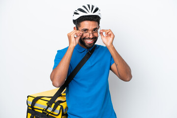 Young Brazilian man with thermal backpack isolated on white background with glasses and surprised