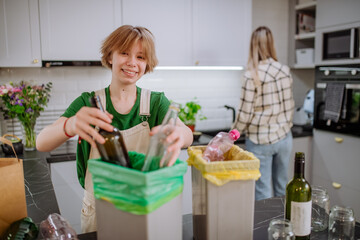 Teen girl throwing glass bottles in recycling bin in the kitchen.