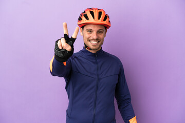 Young Brazilian cyclist man isolated on purple background smiling and showing victory sign - obrazy, fototapety, plakaty