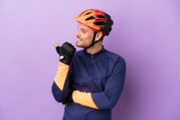 Young Brazilian cyclist man isolated on purple background pointing to the side to present a product