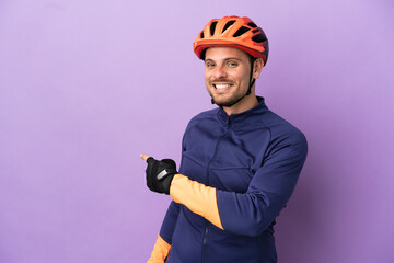 Young Brazilian cyclist man isolated on purple background pointing back
