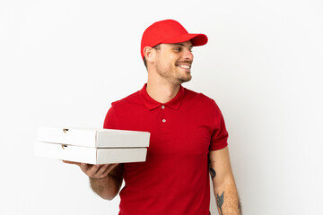 pizza delivery man with work uniform picking up pizza boxes over isolated  white wall looking side