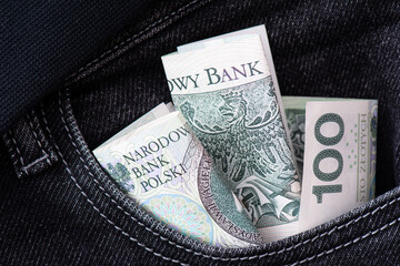 Green cash Paper banknotes one hundred zlotys in the pocket of black jeans. Saving, storing and exchanging money business background.