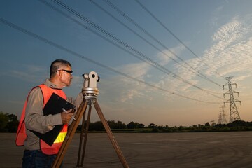 Engineer or surveyor working with theodolite equipment at a field have high voltage in background on sunset time.