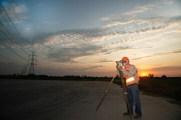 Engineer or surveyor working with theodolite  equipment at a field have high voltage in background at twilight time.