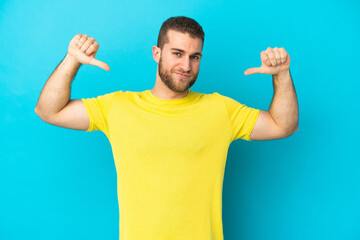 Young handsome caucasian man isolated on blue background proud and self-satisfied