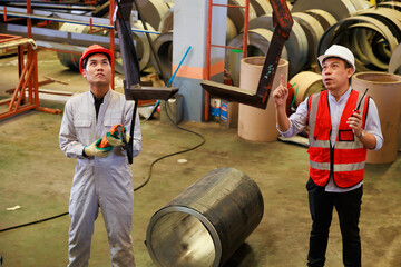 Close up worker hands control indoor overhead crane to lift up metal construction object on metal sheet factory.