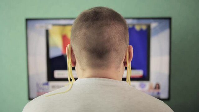 A man with noodles on his ears watches TV. The concept of deception and fakes on the Internet. Unverified Information, news channel