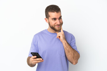 Young handsome caucasian man isolated on white background using mobile phone and thinking