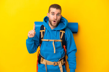 Young caucasian mountaineer man with a big backpack isolated on yellow background thinking an idea pointing the finger up