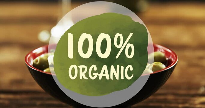 Animation of 100 percent organic text over green olives on wooden background