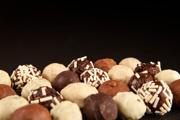 Luxury handmade chocolate bonbon with copy space black or dark background. Assorted pralines with selective focus on black background, close up view.