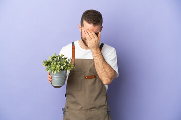 Gardener caucasian man holding a plant isolated on yellow background with tired and sick expression
