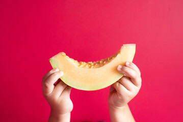 Little child hand holding a honeydew melon or rockmelon against pink background. Concept of healthy eating and agriculture