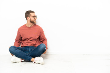 Young handsome man sitting on the floor looking side
