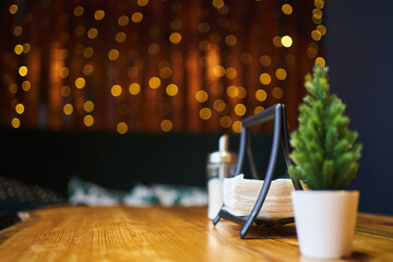 a small christmas tree on a wooden table, napkins in a napkin holder and sugar, blurry lights in the background