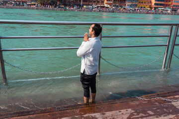 isolated young man prying the holy ganges river at river bank from flat angle