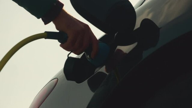 Man opens cap connecting plug to electric car at bright sunlight. Driver charges automobile with alternative energy close low angle shot