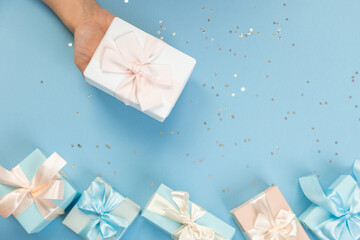 Woman hands holding gift or gift box decorated with confetti on blue pastel table top view. Flat composition for birthday or wedding.