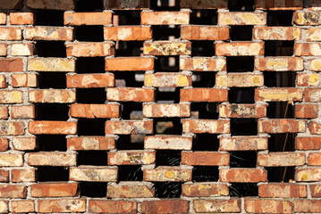 A barn wall made of red bricks with large square holes.